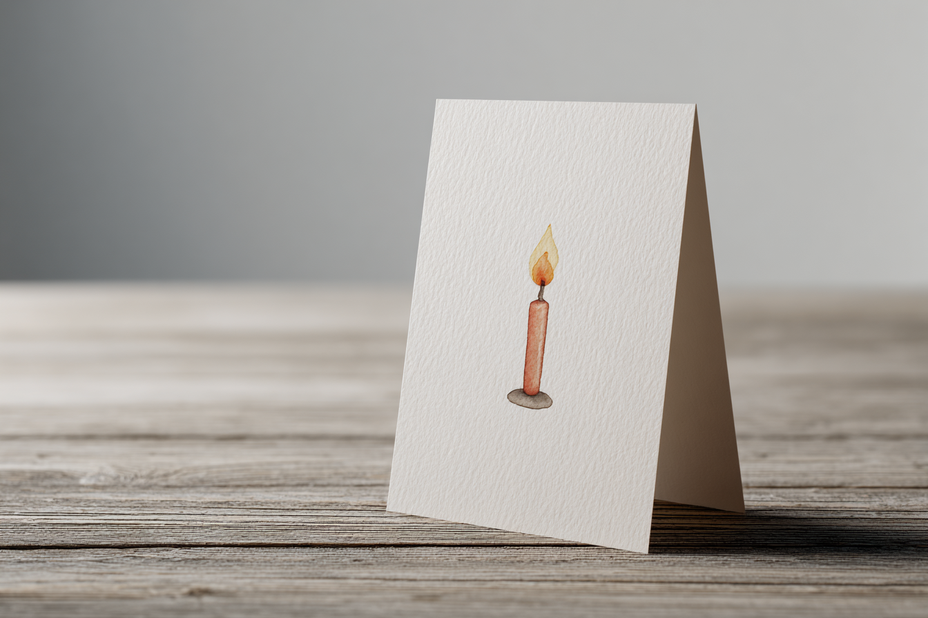A greeting card lying flat, card front showing a single unlit birthday candle