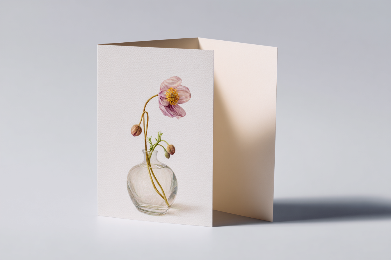 A greeting card lying flat, card front showing a single wilting flower in a glass